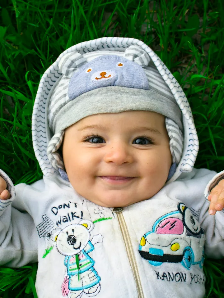 A baby in a grey star-print sleepsuit lying on a bed