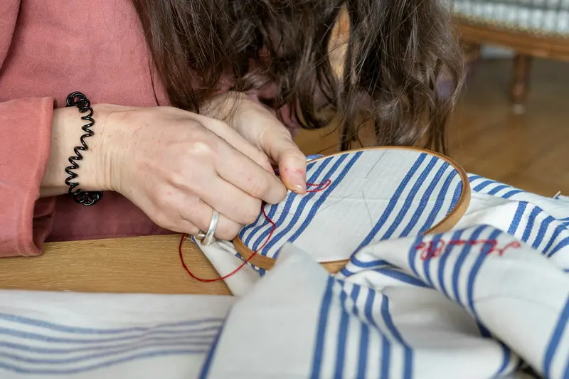 Hands guiding a pale striped cloth under the needle of an embroidery machine