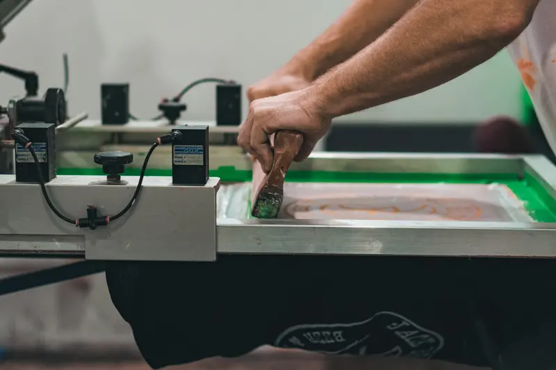 A printer drawing a squeegee across the mesh of a screen-printing carousel