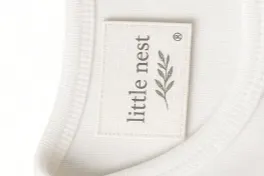 A woven neck label stitched into the back of a white bodysuit, under a soft ribbed neckline