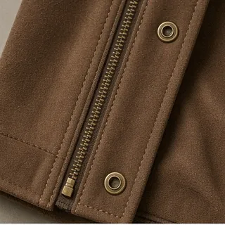 Brass zip and two metal eyelets set into a brown shell, photographed close