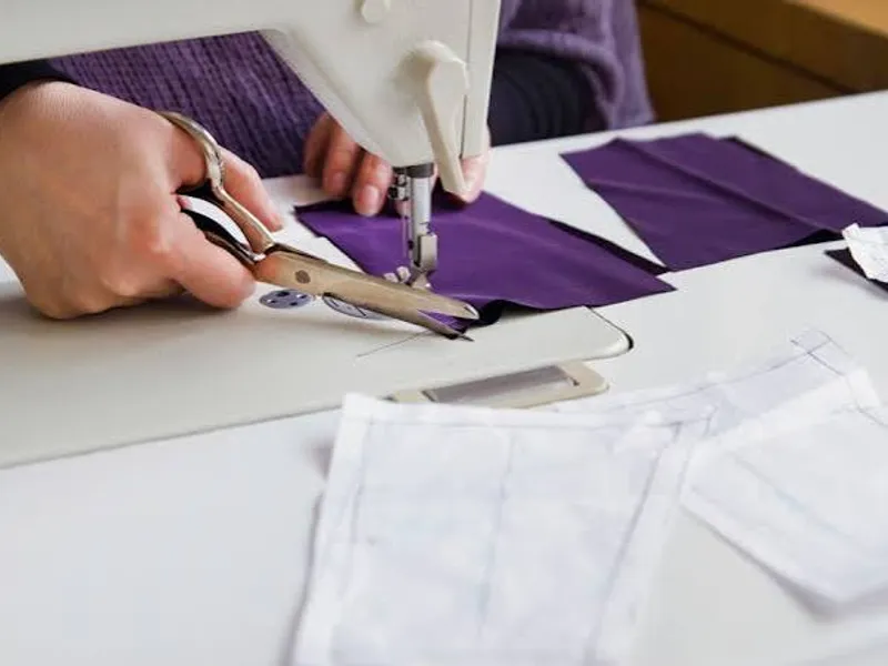 A sewing machine stitching purple fabric on the cut-and-sew line