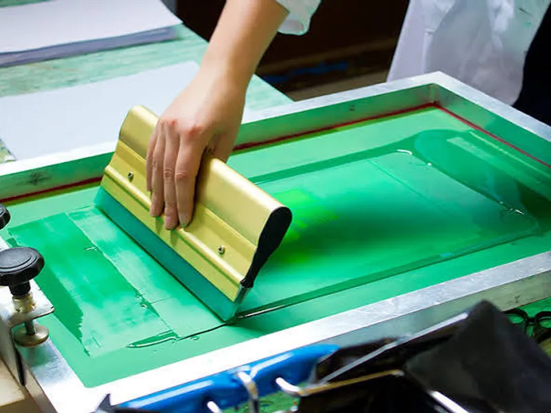 A squeegee pulling ink across a screen — screen printing