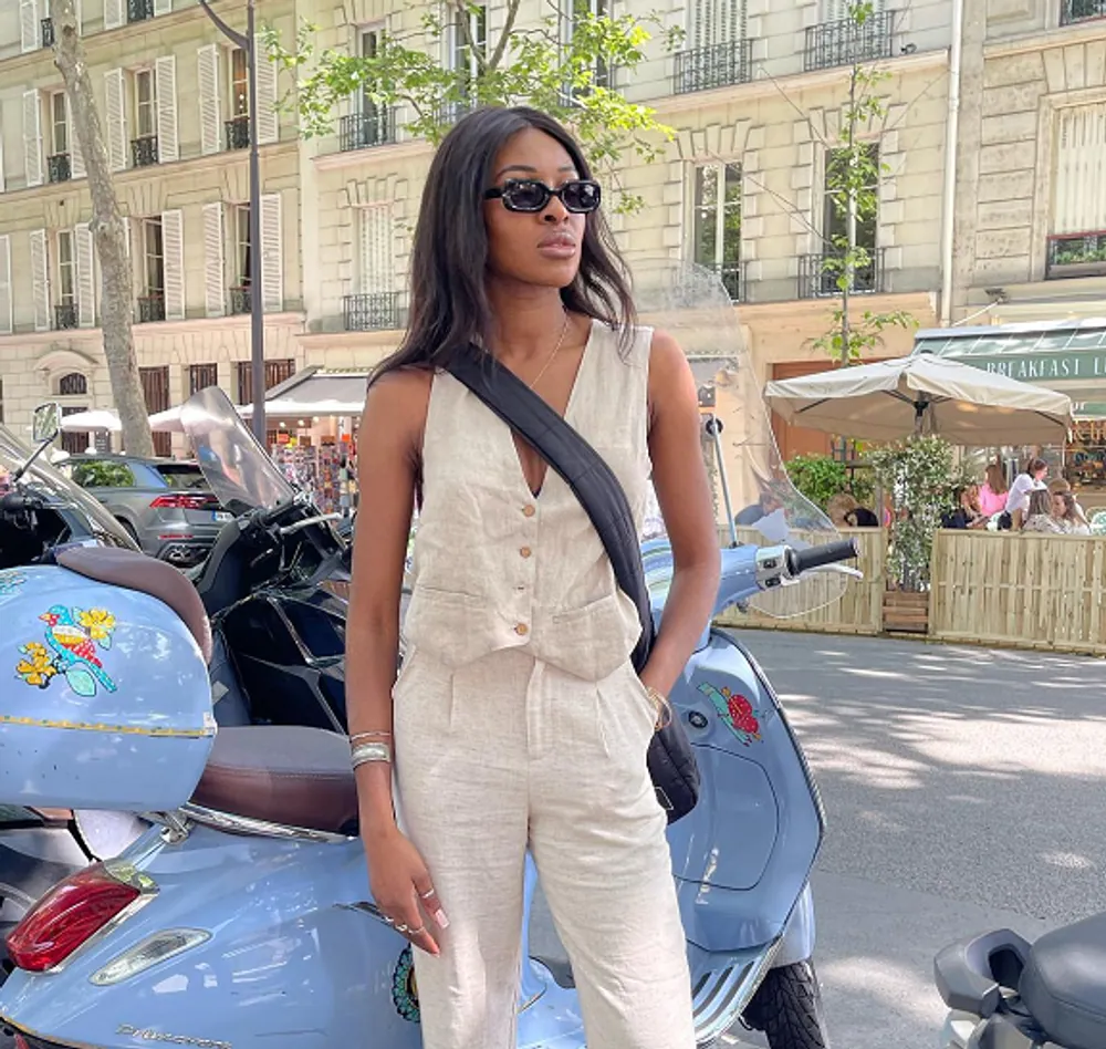 A client in a cream suiting set beside a scooter on a European street