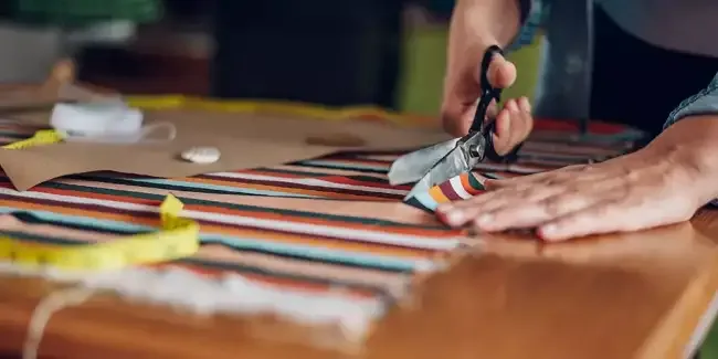 Shears following a chalk line across striped cloth on a wooden cutting table