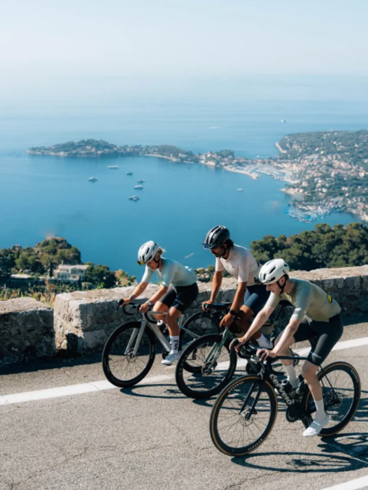 Riding three abreast up a coast road in pale kit, the bay and the far shore dropping away below