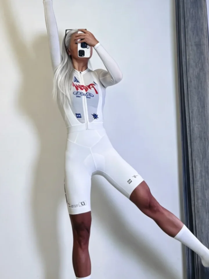 Arm raised in a pale race suit against a plain wall, its chest and both thighs printed
