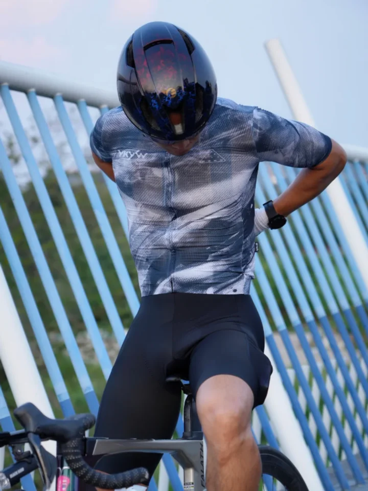 Bent over the bars in a marble-print jersey and a black aero helmet, blue railings behind