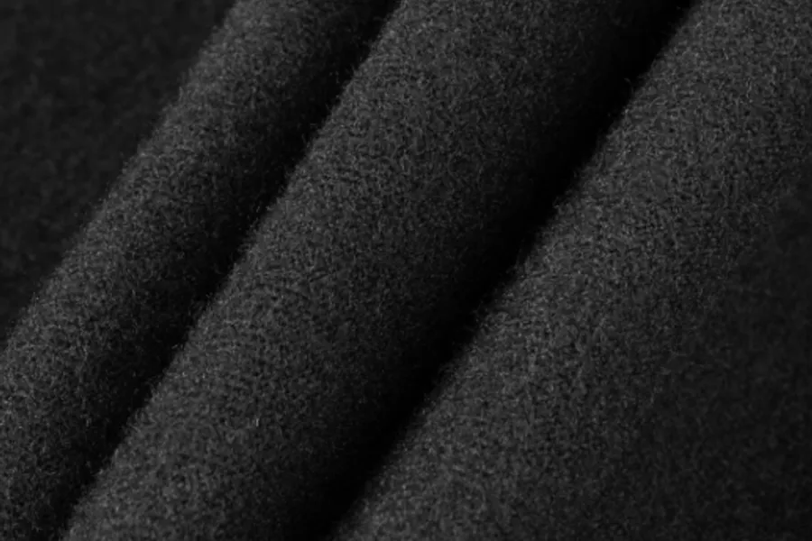 Folded dark fleece filling the frame, its brushed surface catching light along four soft ridges
