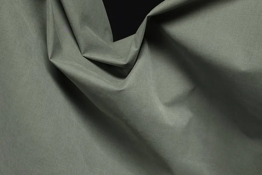 Sage-green shell fabric folded across the frame, its weave catching light along the creases