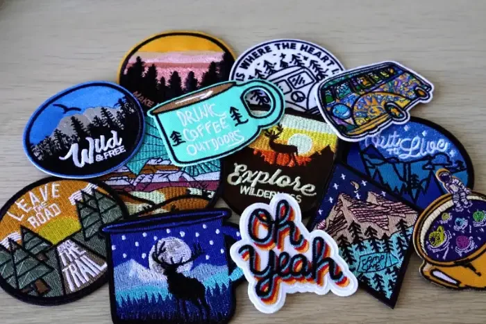 Embroidered patches spread across a table — mountains, a camping mug, a deer and lettering