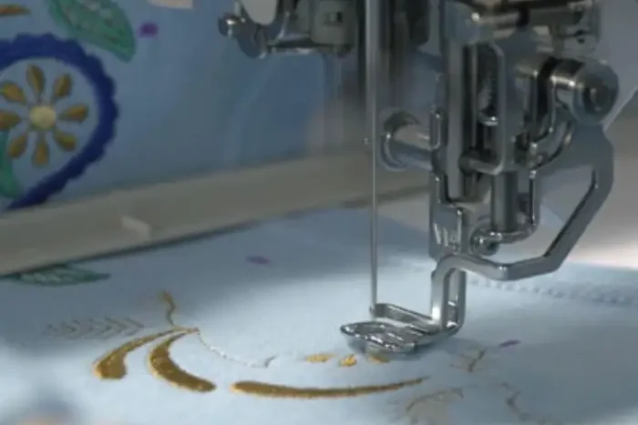 Needle stitching gold thread into pale floral cloth under a machine head