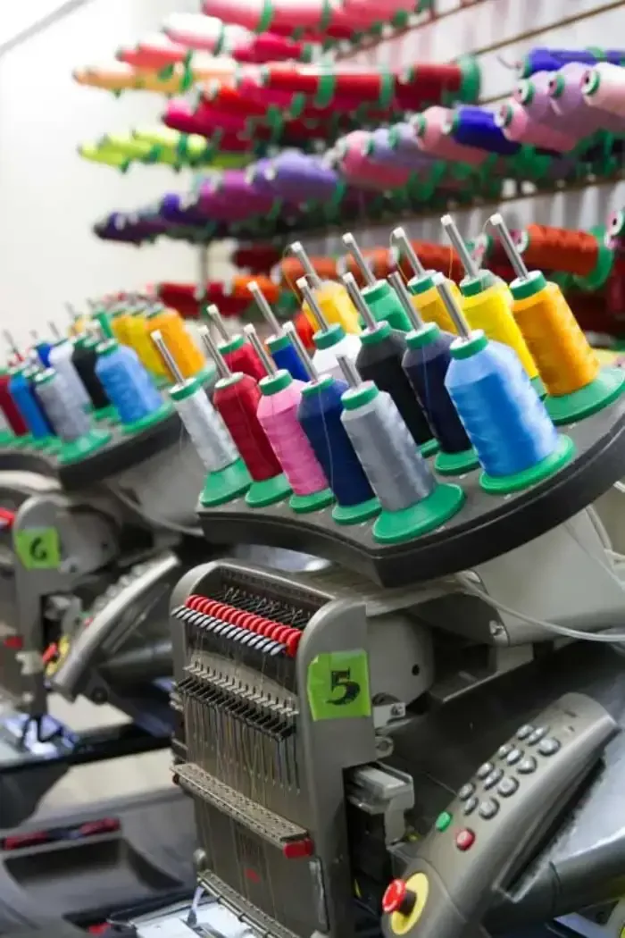 Racks of coloured thread cones above the numbered heads of a multi-needle embroidery machine