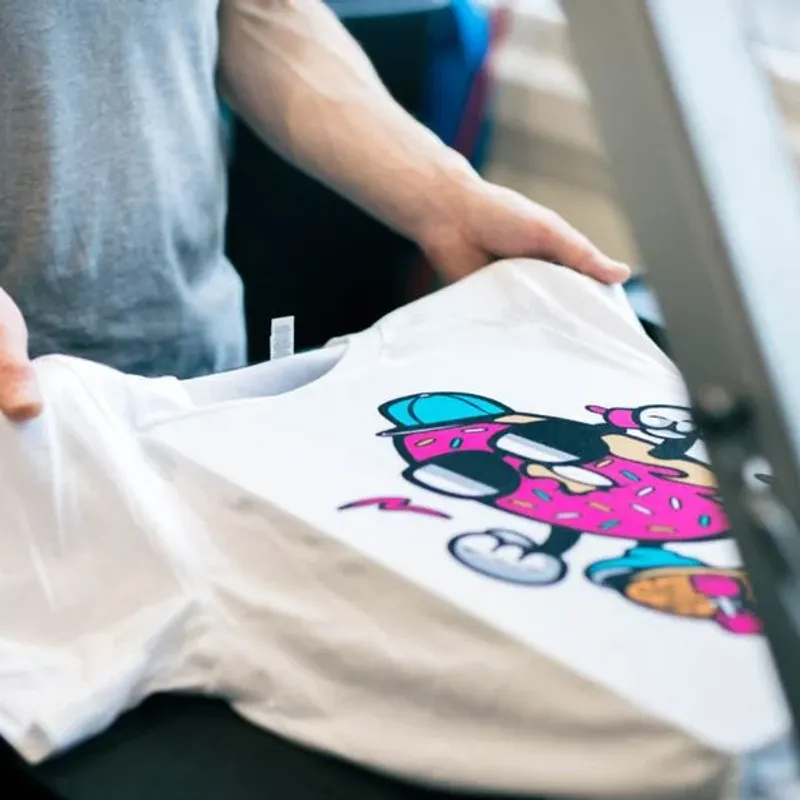Loading a white tee printed with a pink cartoon graphic onto the platen of a DTG machine