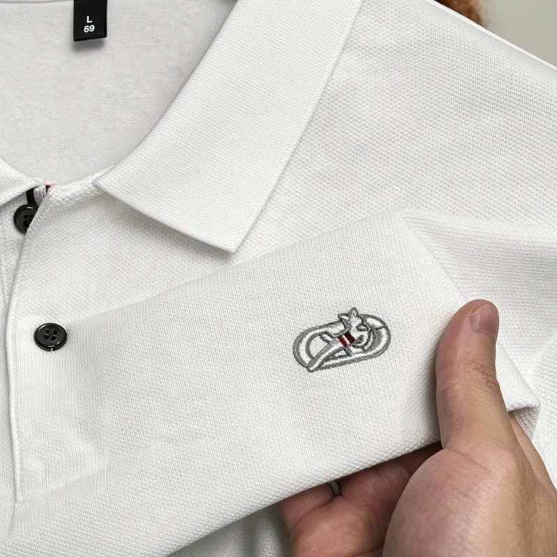 Held open at the placket, a white piqué polo with a silver crest embroidered on the chest