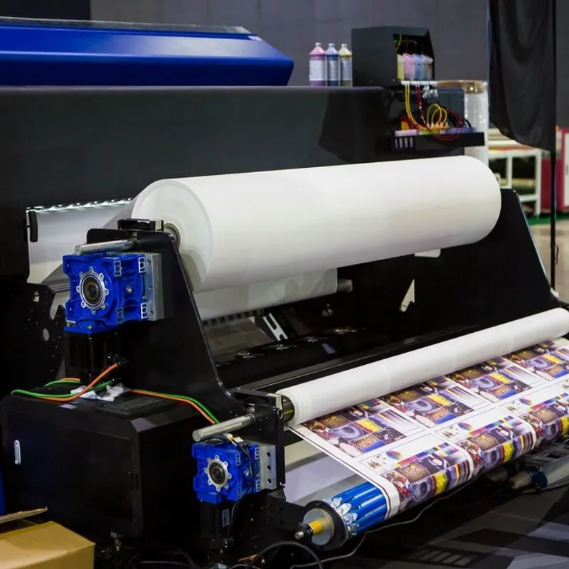 Transfer paper unrolling through a wide-format printer, the printed sheet curling out below