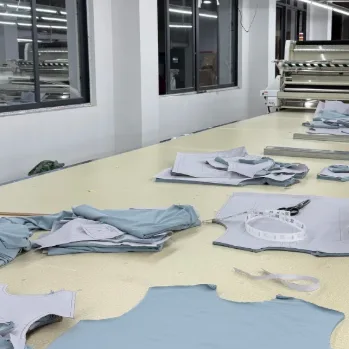 Laid out on a cutting table, layers of pale fabric while a worker runs a straight knife across the stack.