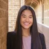 Natalie Reed, in a black blazer over a lilac top, smiling inside a vaulted stone arcade