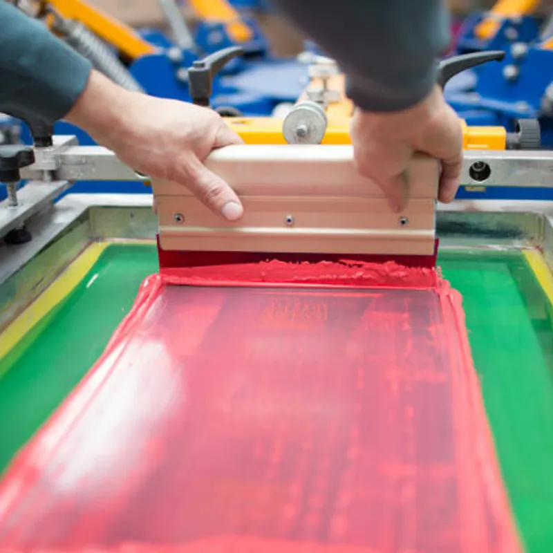 Screen flooding with red ink as a squeegee is pulled across the mesh of a carousel press