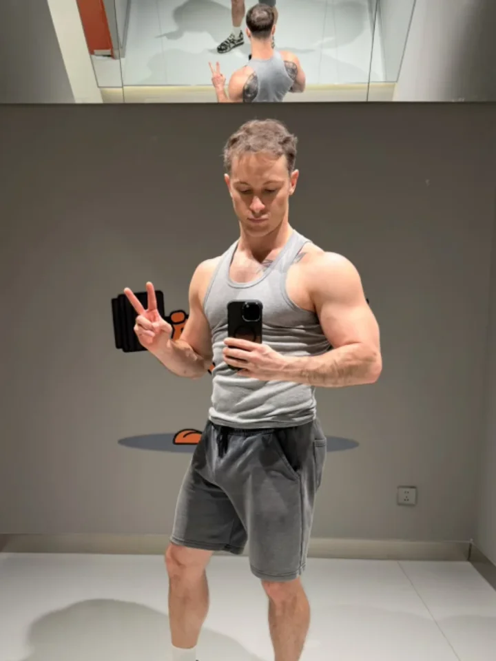Making a peace sign in a grey ribbed tank and shorts, a second phone held up in the other hand