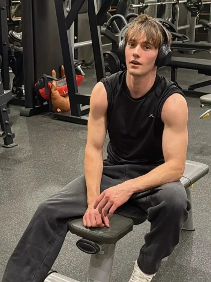 Resting on a bench between sets in a black sleeveless tee, headphones still on