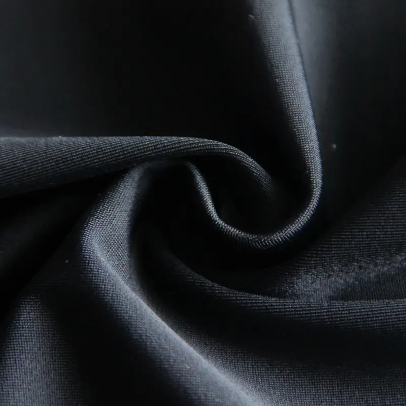 Tightly knitted compression fabric in black, curled to show the dense gauge as a fine even rib