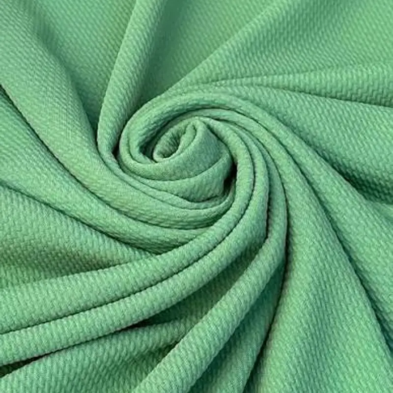 Textured macro of a green four-way stretch knit, swirled into a rosette so the grain reads across the frame