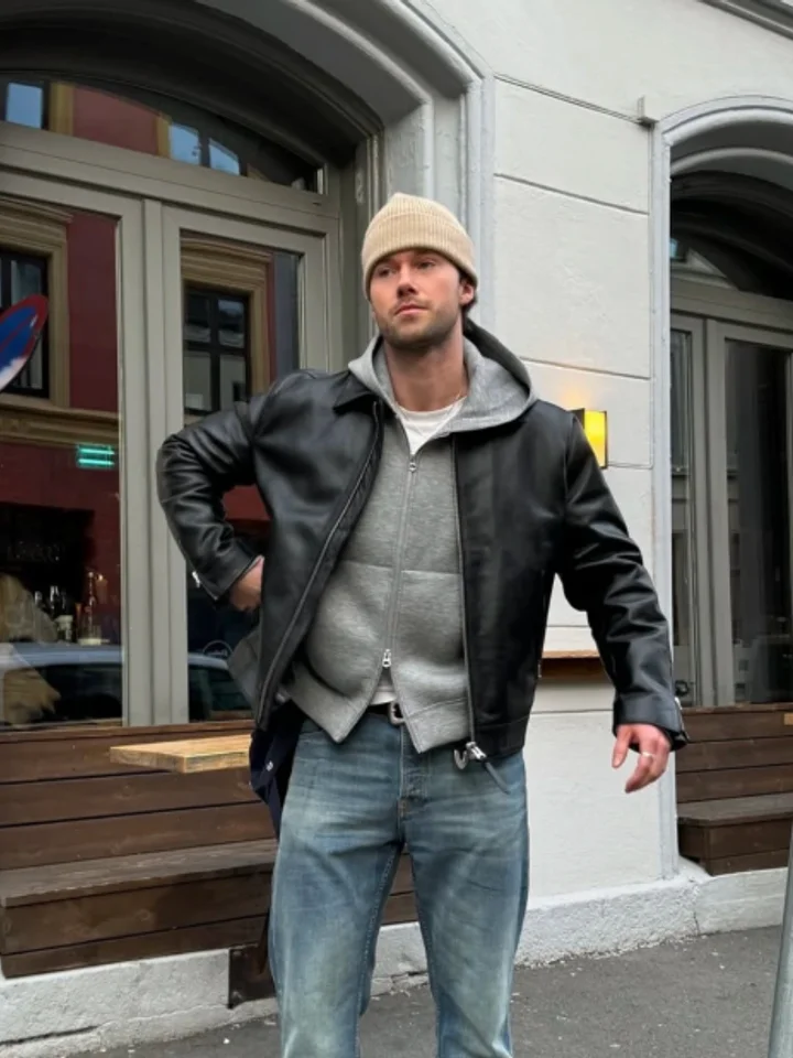 Brown leather jacket over a grey hoodie and a knit cap, on a city street