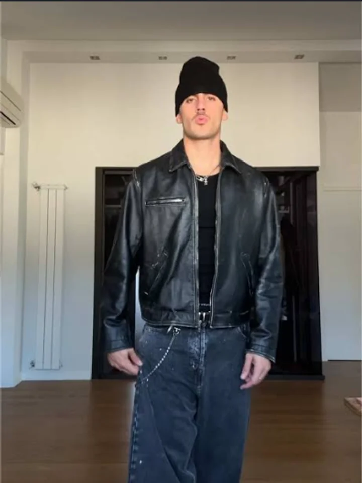 Standing in an empty panelled room in a black leather jacket and beanie