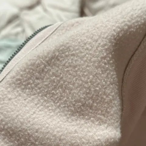 Close-up of a cream micro-fleece backer fabric beside a black jacket zip
