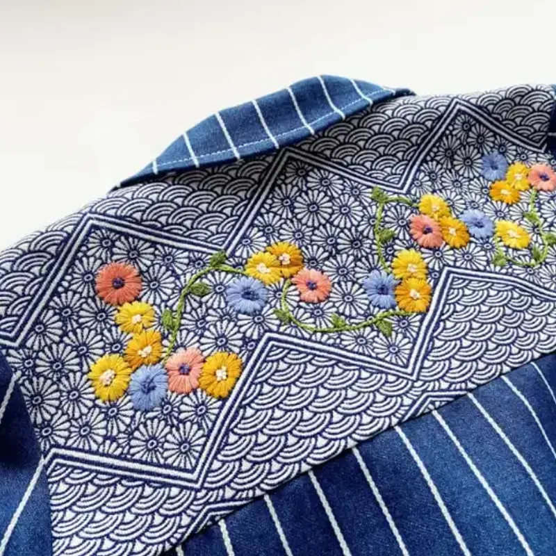 Close-up of a multicolour embroidered flower applied to blue pinstripe fabric