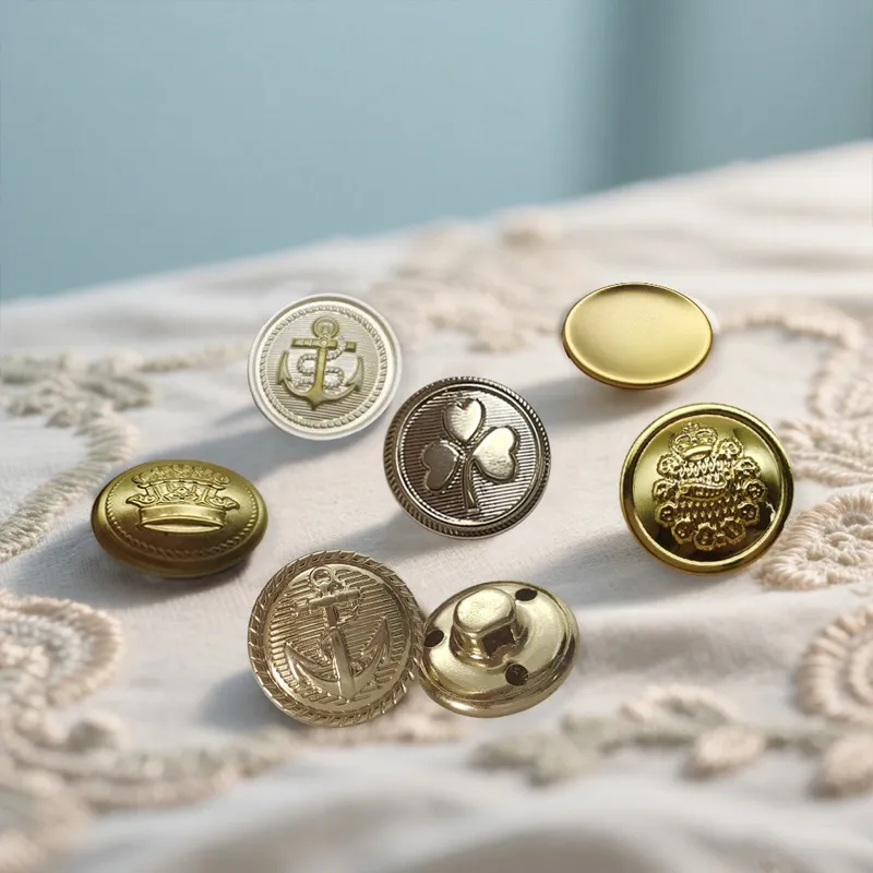 Decorative metal jacket buttons, including anchor, clover, crown and crest designs, scattered on cream embroidered fabric