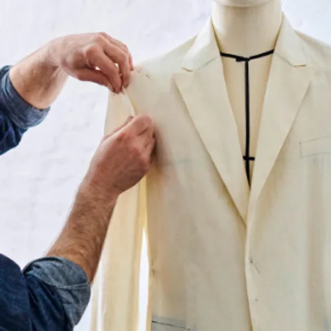Hands adjusting the shoulder seam of a calico toile jacket on a dress form