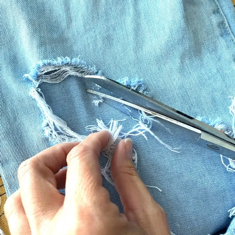 Hands distressing light-blue denim and pulling threads with tweezers