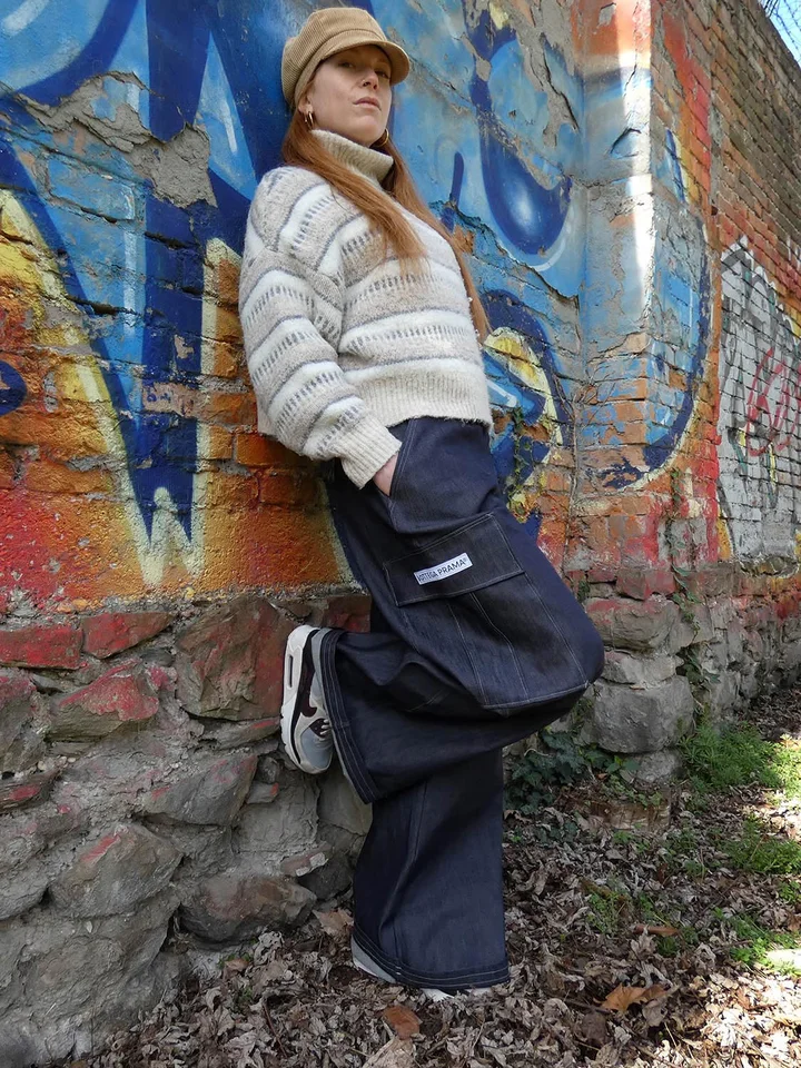 A customer in dark indigo wide-leg cargo jeans and a cream knit sweater against a graffiti wall