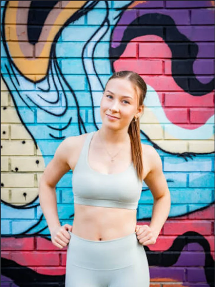 Pale grey seamless sports bra and matching leggings, hands on hips in front of a painted mural