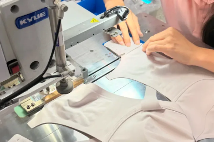Stitching a moulded cup at a sewing station, the padding held flat by hand