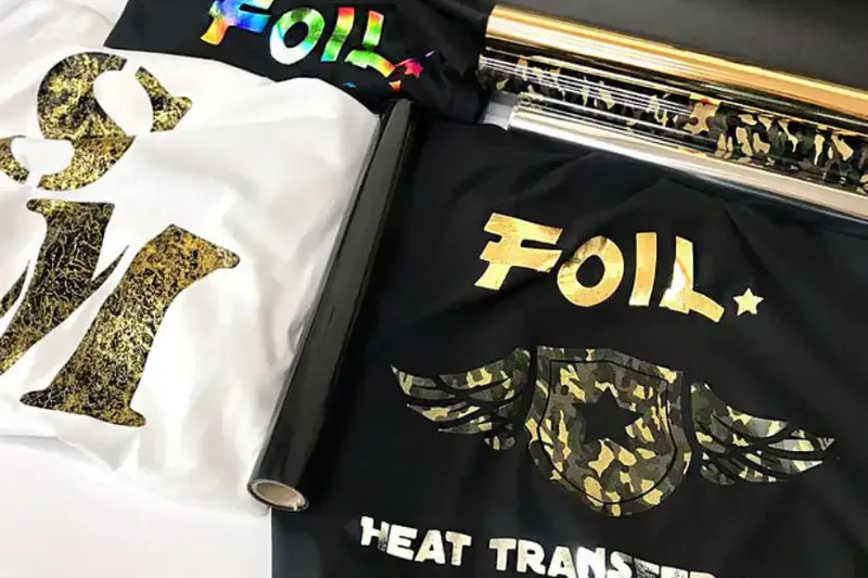 Two flat-laid tees carrying gold and white foil prints beside a heat-transfer label