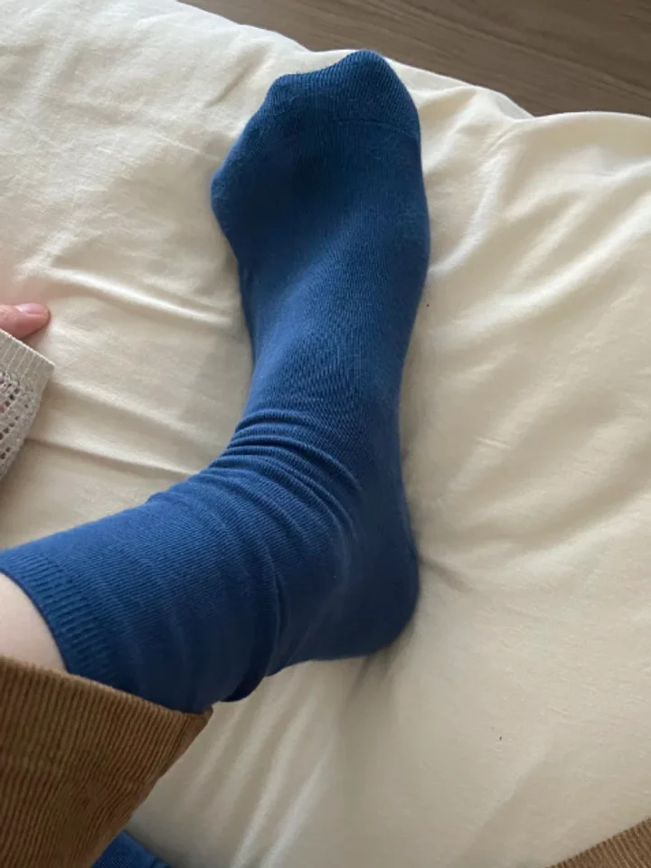 Resting a blue socked foot on rumpled cream linen, a knit sleeve at the edge