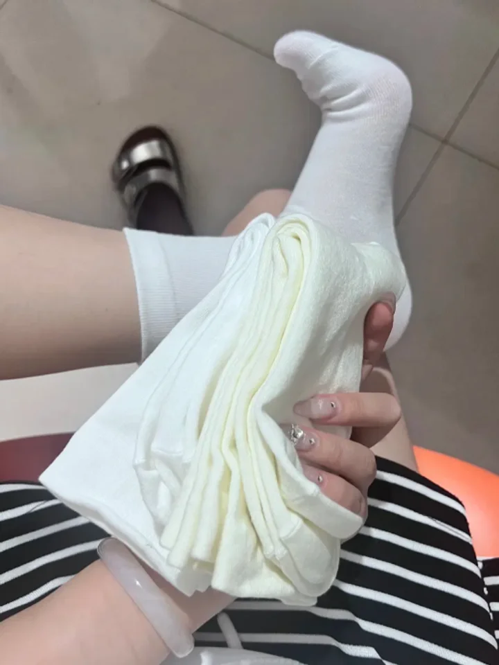Holding a folded cream knit beside a raised white-socked foot on pale tile
