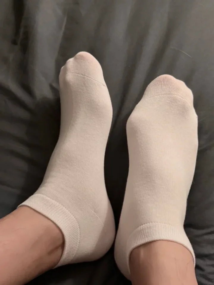Two feet in cream ankle socks against rumpled dark grey bedding