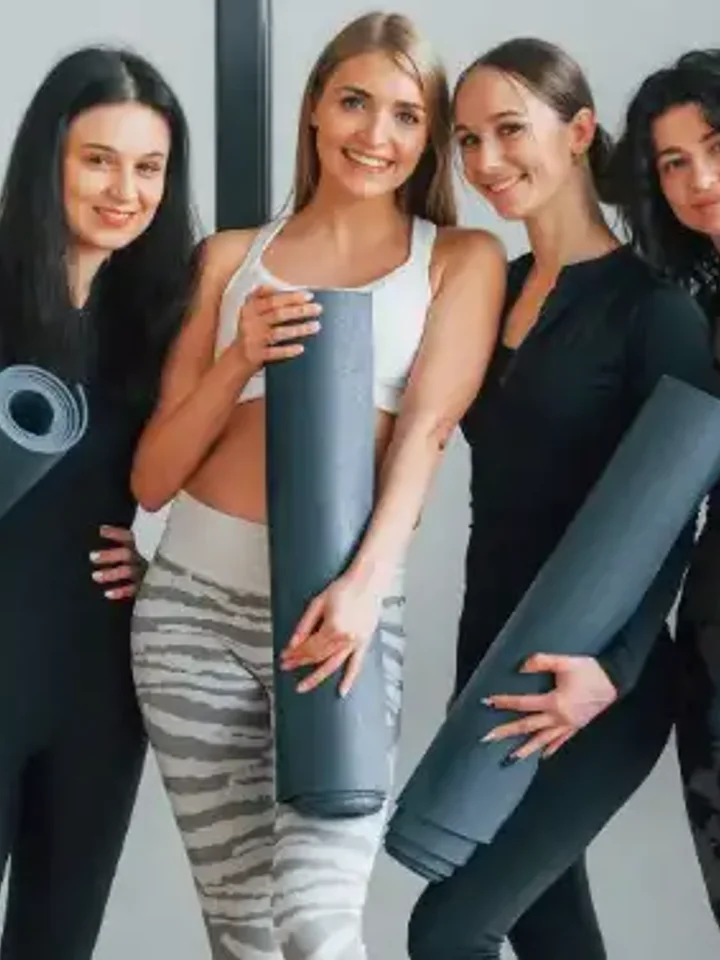 Four women in activewear and leggings holding yoga mats after a class