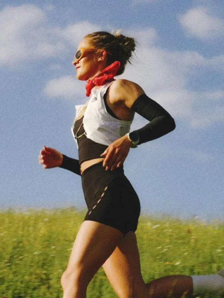 A woman running outdoors in a black crop top, shorts and a red bandana