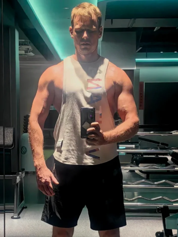 A man in a white training vest and black shorts standing in a gym