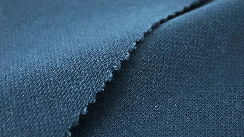 Close-up of a teal recycled performance knit with a stitched seam edge