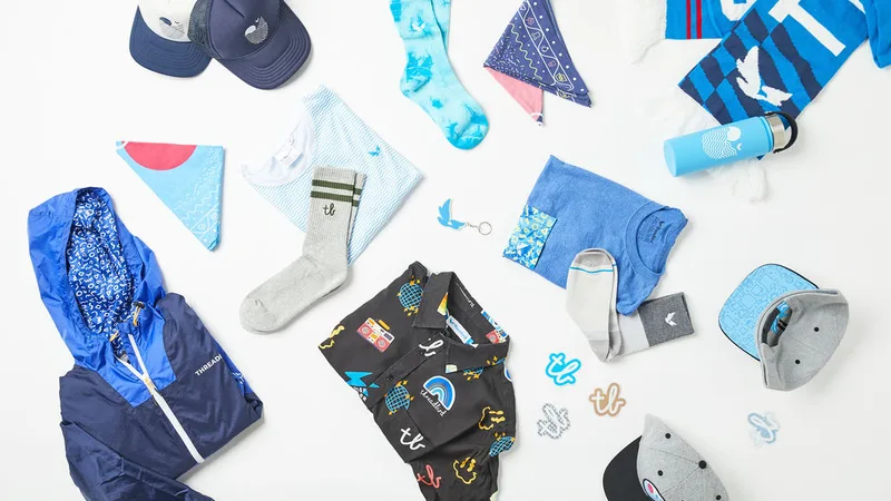 Flat-lay of custom-printed accessories — a jacket, caps, socks, bandanas, tees and a bottle — on a white ground