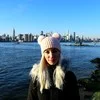 Portrait of a woman in a pink knitted hat with a city skyline across the water behind her