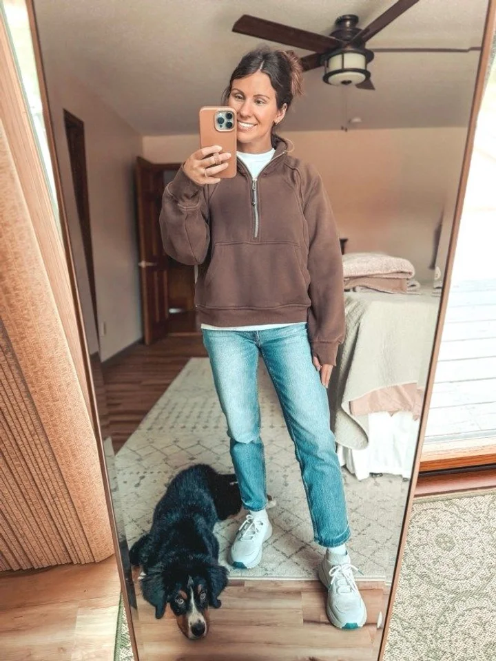 A customer taking a mirror selfie in a brown half-zip sweatshirt and jeans