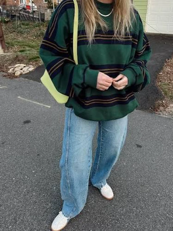 A customer in an oversized green and navy striped sweatshirt and wide jeans, carrying a yellow tote