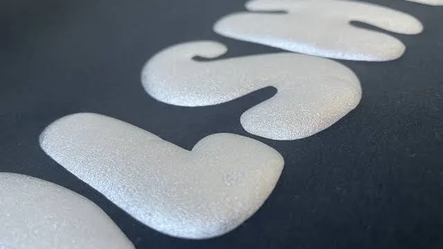 Raised white puff-print lettering on a black garment, shot at a low angle